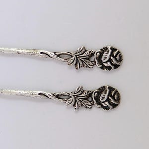 May include: Two silver teaspoons with rose-shaped handles. The handles are intricately detailed with leaves and flowers.