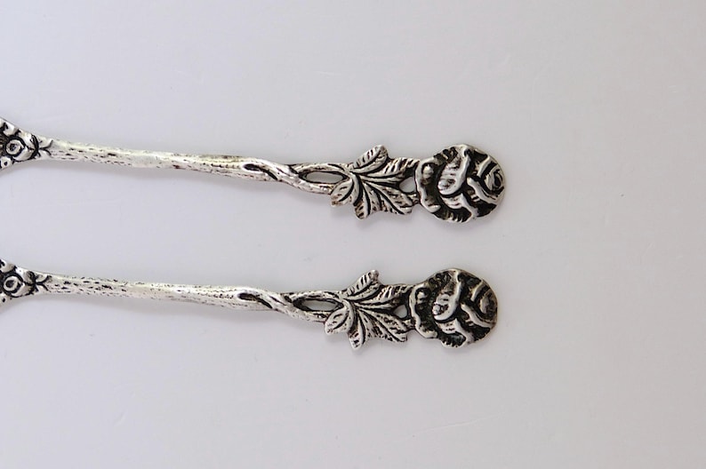 May include: Two silver teaspoons with rose-shaped handles. The handles are intricately detailed with leaves and flowers.