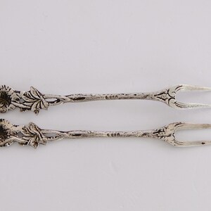 May include: A pair of silver-plated serving forks with ornate floral designs. The forks have two tines and are marked with "800" on the back.