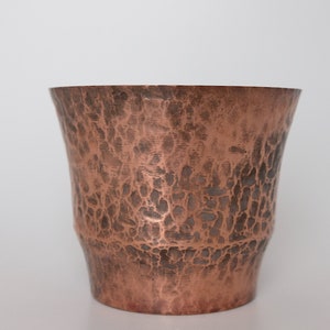 May include: A hammered copper cup with a textured surface. The cup is a light brown color and has a rounded bottom.