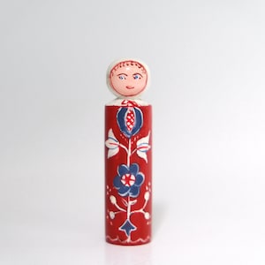 Könnte beinhalten: Eine handbemalte Holzpuppe mit rotem und weißem Blumendesign. Die Puppe hat einen runden Kopf mit bemaltem Gesicht und einen weißen Körper.