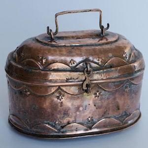 May include: An antique copper box with a hinged lid and a decorative handle. The box has a worn, aged patina and intricate floral designs.