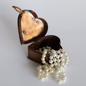 May include: An open heart-shaped box made of copper with a pearl necklace spilling out of it.