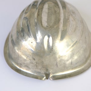 K&ouml;nnte beinhalten: Eine silberne Metallform zum Backen eines Kuchens oder Desserts. Die Form hat ein geriffeltes Design und ist kuppelf&ouml;rmig.