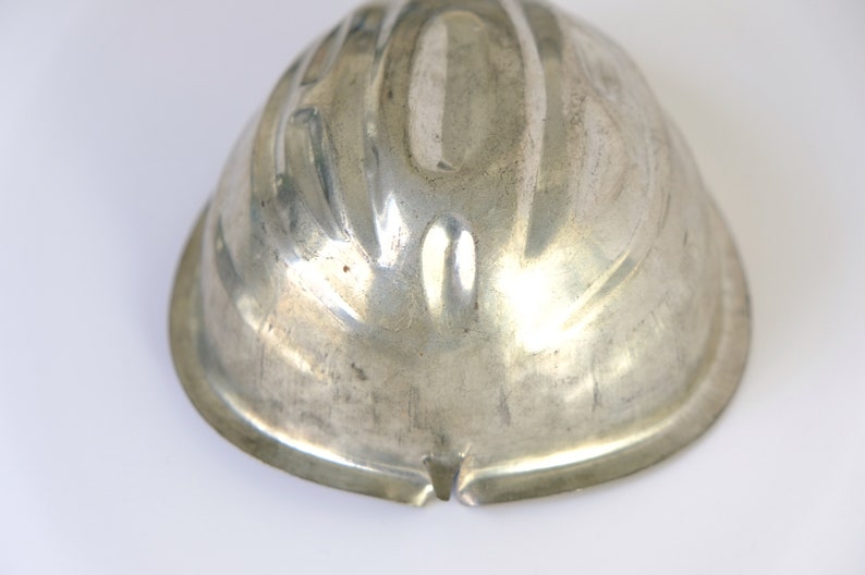 K&ouml;nnte beinhalten: Eine silberne Metallform zum Backen eines Kuchens oder Desserts. Die Form hat ein geriffeltes Design und ist kuppelf&ouml;rmig.