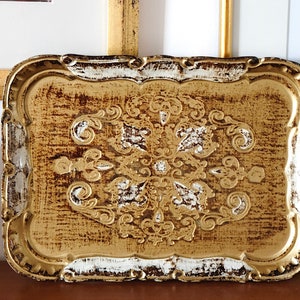 May include: A gold and white decorative tray with a distressed finish and an ornate design. The tray has a rectangular shape with a slightly raised edge.
