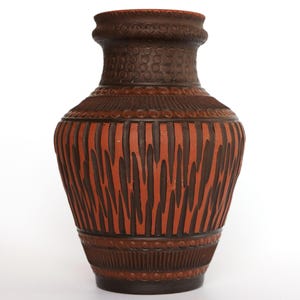 May include: A tall, brown ceramic vase with a textured surface. The vase features a reddish-brown body with vertical dark brown stripes and a detailed, patterned neck and base. The vase is approximately 12 inches tall.