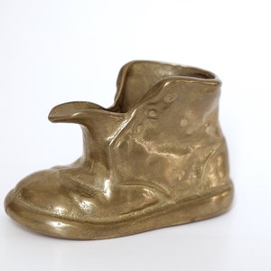 Könnte beinhalten: Ein Aschenbecher aus Messing in Form eines Stiefels. Der Stiefel hat ein detailliertes Design und eine abgenutzte Oberfläche.