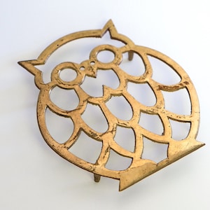 May include: Gold metal owl-shaped hot pad with a decorative cut-out design.