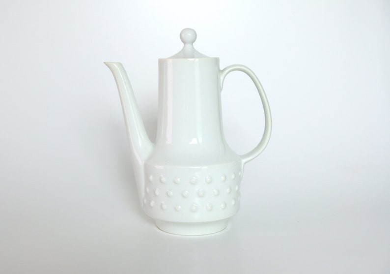 May include: White ceramic coffee pot with a round lid and a textured base. The pot has a spout and a handle.