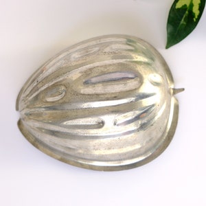 K&ouml;nnte beinhalten: Eine silberne Metallform in Form einer halben Melone. Die Form hat eine gerippte Textur und einen glatten, abgerundeten Rand.