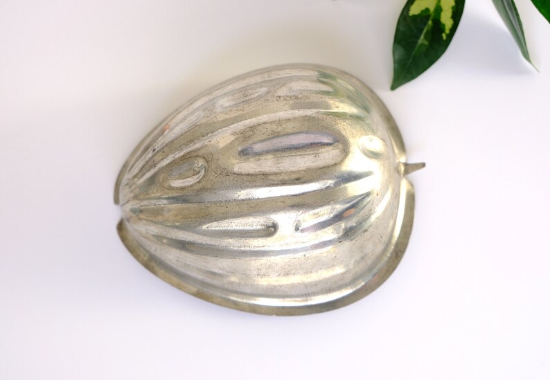 K&ouml;nnte beinhalten: Eine silberne Metallform in Form einer halben Melone. Die Form hat eine gerippte Textur und einen glatten, abgerundeten Rand.