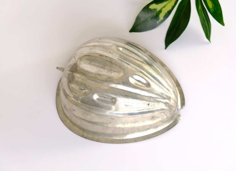 K&ouml;nnte beinhalten: Eine silberne Metallform in Form einer halben Melone. Die Form hat eine gerippte Textur und ist zum Herstellen von Desserts gedacht.