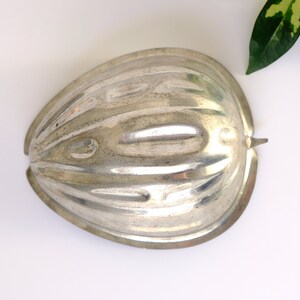 K&ouml;nnte beinhalten: Silberne Metallform in Form einer halben, halbierten Frucht mit gerippter Textur.