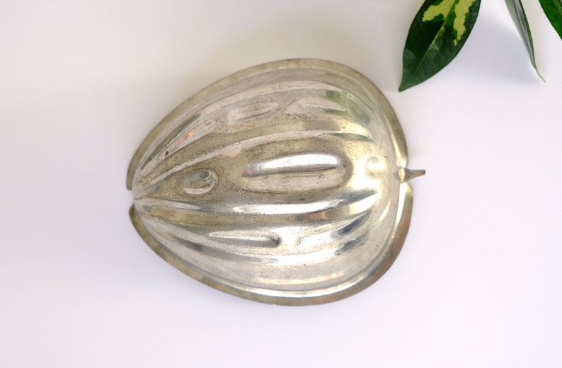 K&ouml;nnte beinhalten: Silberne Metallform in Form einer halben, halbierten Frucht mit gerippter Textur.