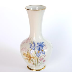 Könnte beinhalten: Eine weiße Porzellanvase mit goldenem Rand und Boden. Die Vase hat ein Blumendesign mit blauen, gelben und rosa Irisblüten. Die Vase hat einen schlanken Hals und einen leicht ausgestellten Boden, etwa 20 cm hoch.