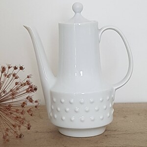 May include: White ceramic coffee pot with a round lid and a textured base. The pot has a spout and a handle.