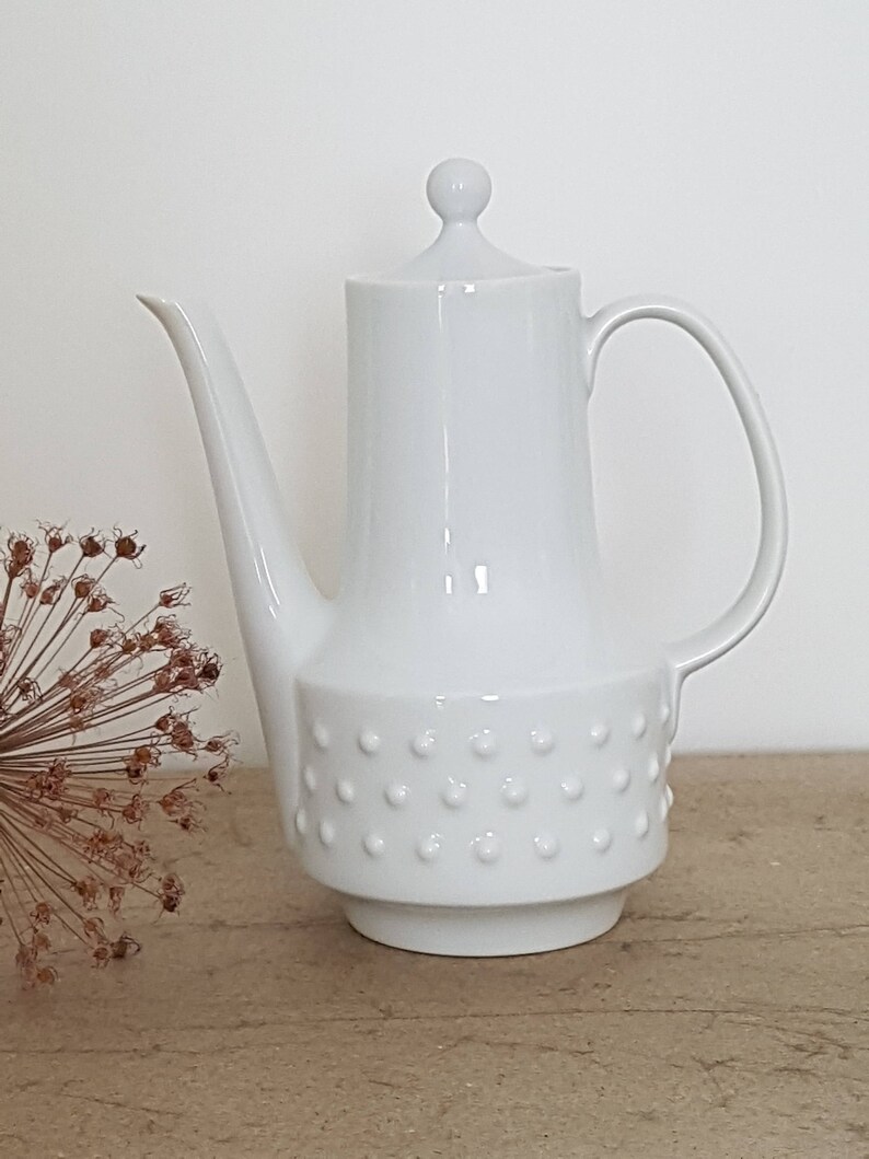 May include: White ceramic coffee pot with a round lid and a textured base. The pot has a spout and a handle.