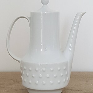 May include: White ceramic coffee pot with a textured, dotted design on the bottom half. The pot has a lid with a knob on top.