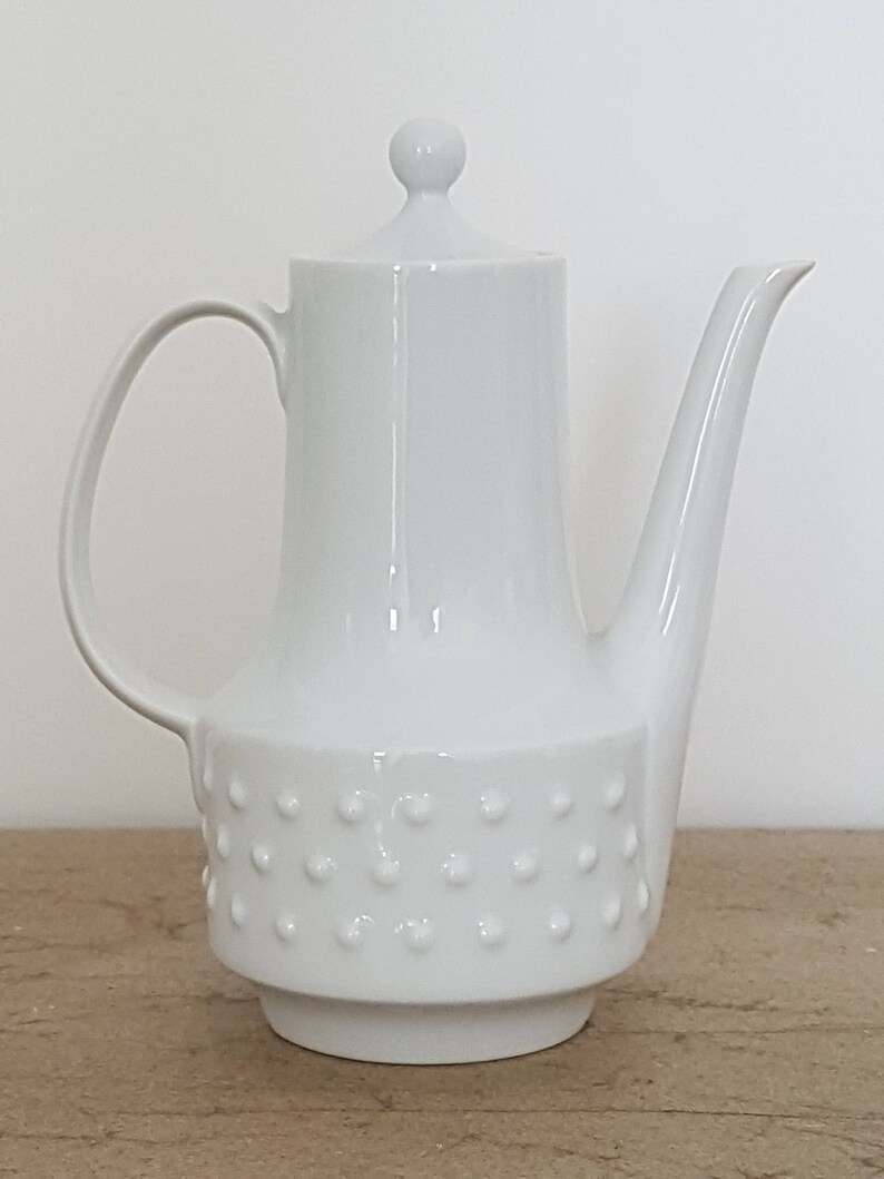 May include: White ceramic coffee pot with a textured, dotted design on the bottom half. The pot has a lid with a knob on top.