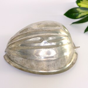 K&ouml;nnte beinhalten: Eine silberne Metallform zum Backen eines Kuchens oder Desserts in Form eines halben Herzens. Die Form hat eine strukturierte Oberfl&auml;che und ist so konzipiert, dass sie einen dekorativen, geriffelten Rand erzeugt.