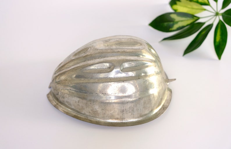 K&ouml;nnte beinhalten: Eine silberne Metallform zum Backen eines Kuchens oder Desserts in Form eines halben Herzens. Die Form hat eine strukturierte Oberfl&auml;che und ist so konzipiert, dass sie einen dekorativen, geriffelten Rand erzeugt.