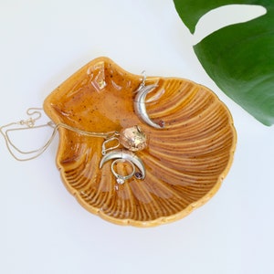 May include: A ceramic seashell dish in a brown glaze with a gold chain necklace and silver earrings inside.