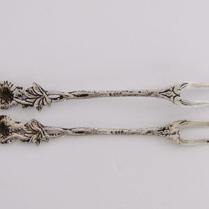 May include: Two silver forks with floral designs on the handles. The forks are about 5 inches long.