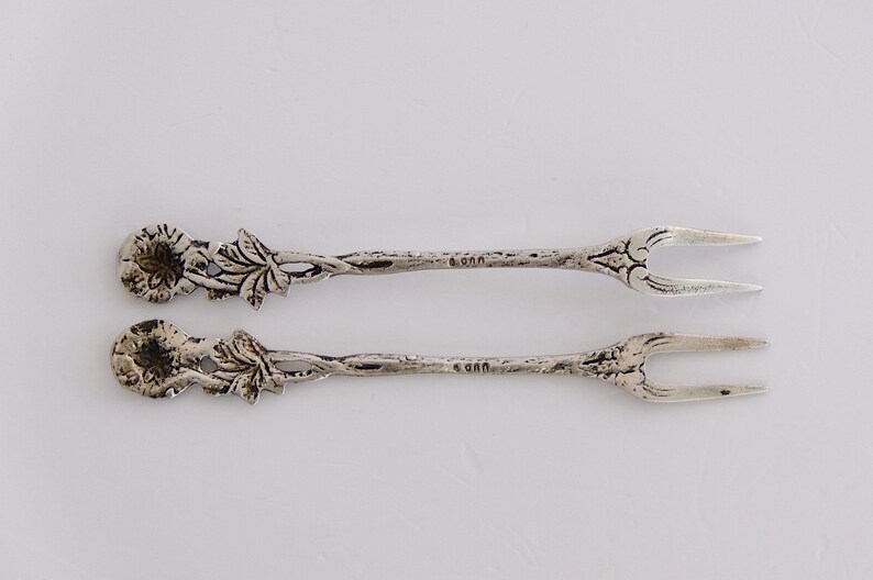 May include: Two silver forks with floral designs on the handles. The forks are about 5 inches long.
