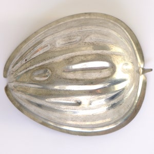 K&ouml;nnte beinhalten: Eine silberne Metallform in Form einer halben Melone. Die Form hat eine gerippte Textur und einen glatten, abgerundeten Rand.