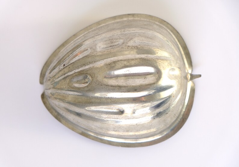 K&ouml;nnte beinhalten: Eine silberne Metallform in Form einer halben Melone. Die Form hat eine gerippte Textur und einen glatten, abgerundeten Rand.