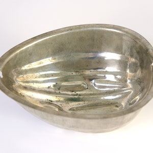 K&ouml;nnte beinhalten: Eine silberne Metallform in Form einer halben Eiform mit gerippter Textur.
