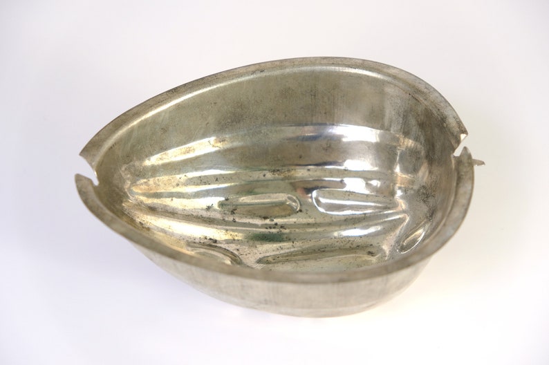K&ouml;nnte beinhalten: Eine silberne Metallform in Form einer halben Eiform mit gerippter Textur.