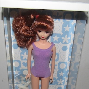 May include: A purple swimsuit doll with brown hair in a ponytail. The doll is in a clear plastic display case with a blue and white background. The packaging includes the text "TAKARA-BAKO ORIGINAL DOLL" and "創作・著作物 TAKARA CO,LTD. 2001 タカラ".