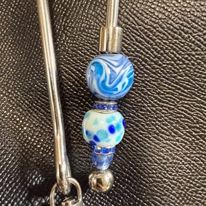 May include: A silver key chain with a blue and white glass bead and a silver clasp.