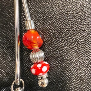 May include: A silver bag charm with a hook, a silver bead, a red and orange glass bead, and a red glass bead with white polka dots.