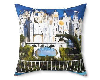 May include: A blue and white throw pillow with a watercolor painting of a whimsical building with multiple clocks and a blue sky. The building is surrounded by green bushes and a white fence.