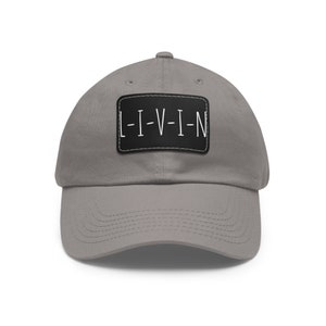 May include: A grey baseball cap with a black patch that says "L-I-V-I-N" in white lettering.