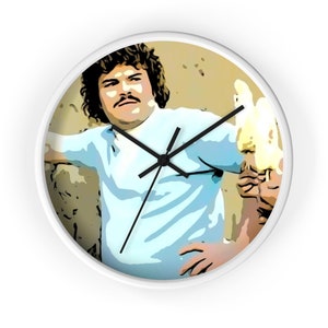 May include: A white wall clock featuring a cartoon illustration of a man with brown hair, a mustache, and a blue shirt. He is holding a lit match in his right hand. The background is a light brown color.
