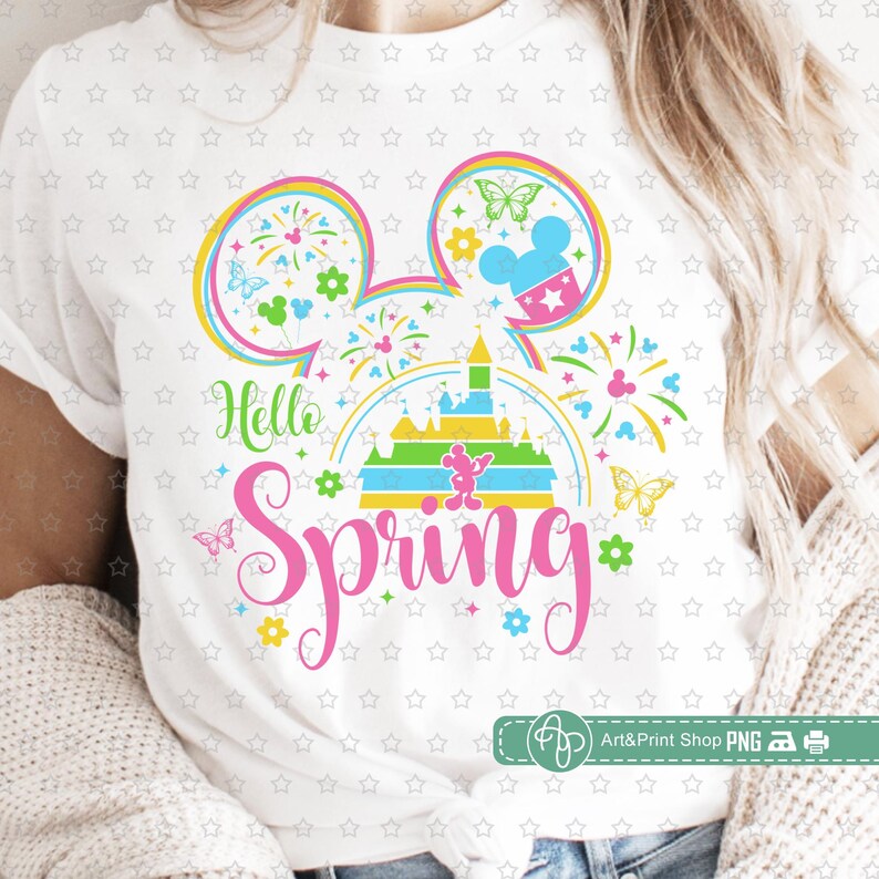 May include: A white t-shirt with a colorful graphic design featuring Mickey Mouse ears, a rainbow, fireworks, and the text "Hello Spring".