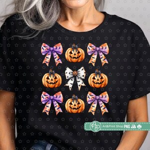 May include: A black t-shirt with a repeating pattern of orange pumpkins with purple and orange bows. The pumpkins have a jack-o-lantern face.
