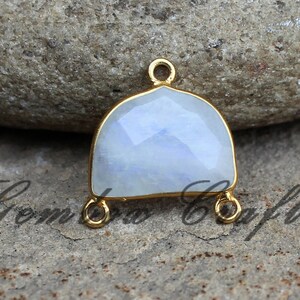 May include: Gold-plated pendant with a white moonstone gemstone. The pendant has three loops for attaching to a chain or cord.