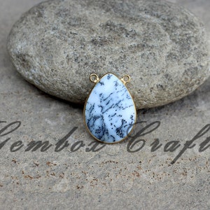 May include: A white and black dendritic agate pendant with gold-tone bail. The pendant is shaped like a teardrop and has a natural, organic look.