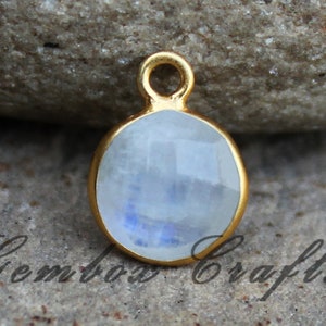 Puede incluir: Pendiente chapado en oro con una piedra de luna redonda blanca con un brillo azul iridiscente.