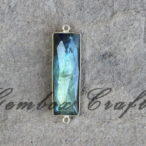 Peut inclure: Un pendentif doré avec une pierre rectangulaire en labradorite bleu et vert irisé. Le pendentif a deux anneaux de saut pour l'attacher à une chaîne.