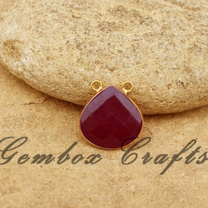 Puede incluir: Un colgante en forma de lágrima con una piedra preciosa roja oscura engastada en oro.