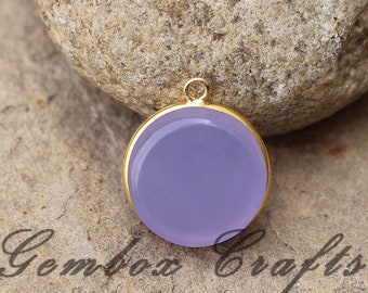 May include: A round, purple gemstone pendant with a gold-toned bezel setting. The pendant is on a rough, brown surface.