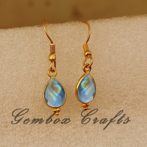 Puede incluir: Un par de pendientes de aro dorados con piedras azules iridiscentes en forma de lágrima.