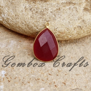 Peut inclure: Un pendentif en forme de larme en pierre rouge avec un sertissage doré. Le pendentif est facetté.