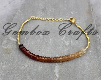 May include: A gold bracelet with a graduated ombre effect of brown and light brown gemstone beads.